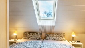 A bedroom with a skylight, two bedside lamps, a bed with patterned bedding, and a nightstand with a lamp and a remote control. - Meeresfeeling for 2: Cozy North Sea Apartment, 34 sqm, 1 Bedroom, Max 2 Guests (Horumersiel)