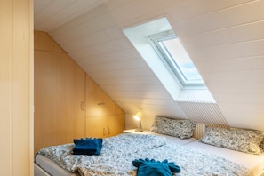 Une chambre avec un plafond en pente, un puits de lumière, un lit avec une literie à motifs et une lampe de chevet.
