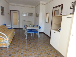 Une pièce de taille modeste comprenant un lit, une table à manger avec des chaises, une petite kitchenette et une armoire.