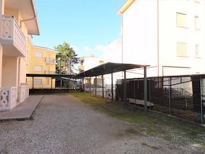 Une cour avec un chemin de gravier, des espaces de repos abrités et un espace de stationnement pour vélos délimité par une clôture.