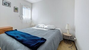 A bedroom with a bed, two bedside lamps, a window with curtains, and a small round table with a lamp. - Bright apartment near beach (Narbonne)