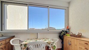 A small kitchen with a table and chairs, a window with a view, and wooden cabinets. - Bright apartment near beach (Narbonne)
