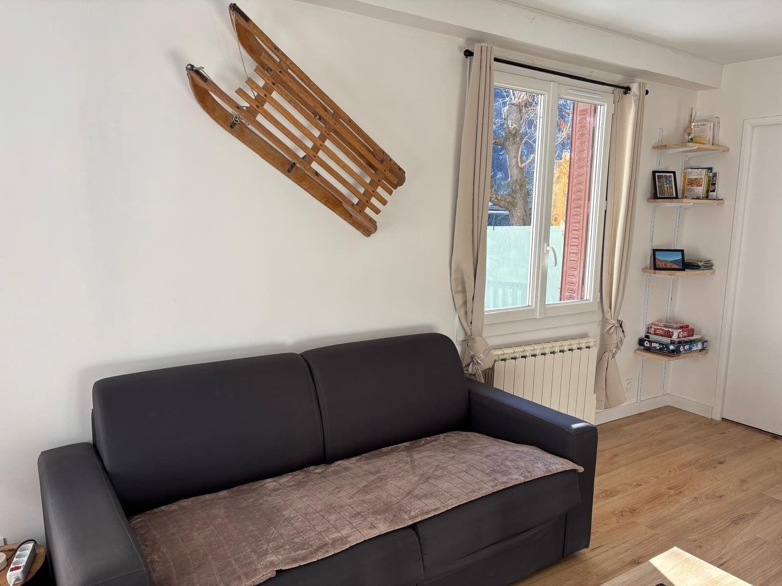 Ein Wohnzimmer mit einer schwarzen Couch, einem Holzlager, einem Fenster mit Vorhängen und einer Heizung.