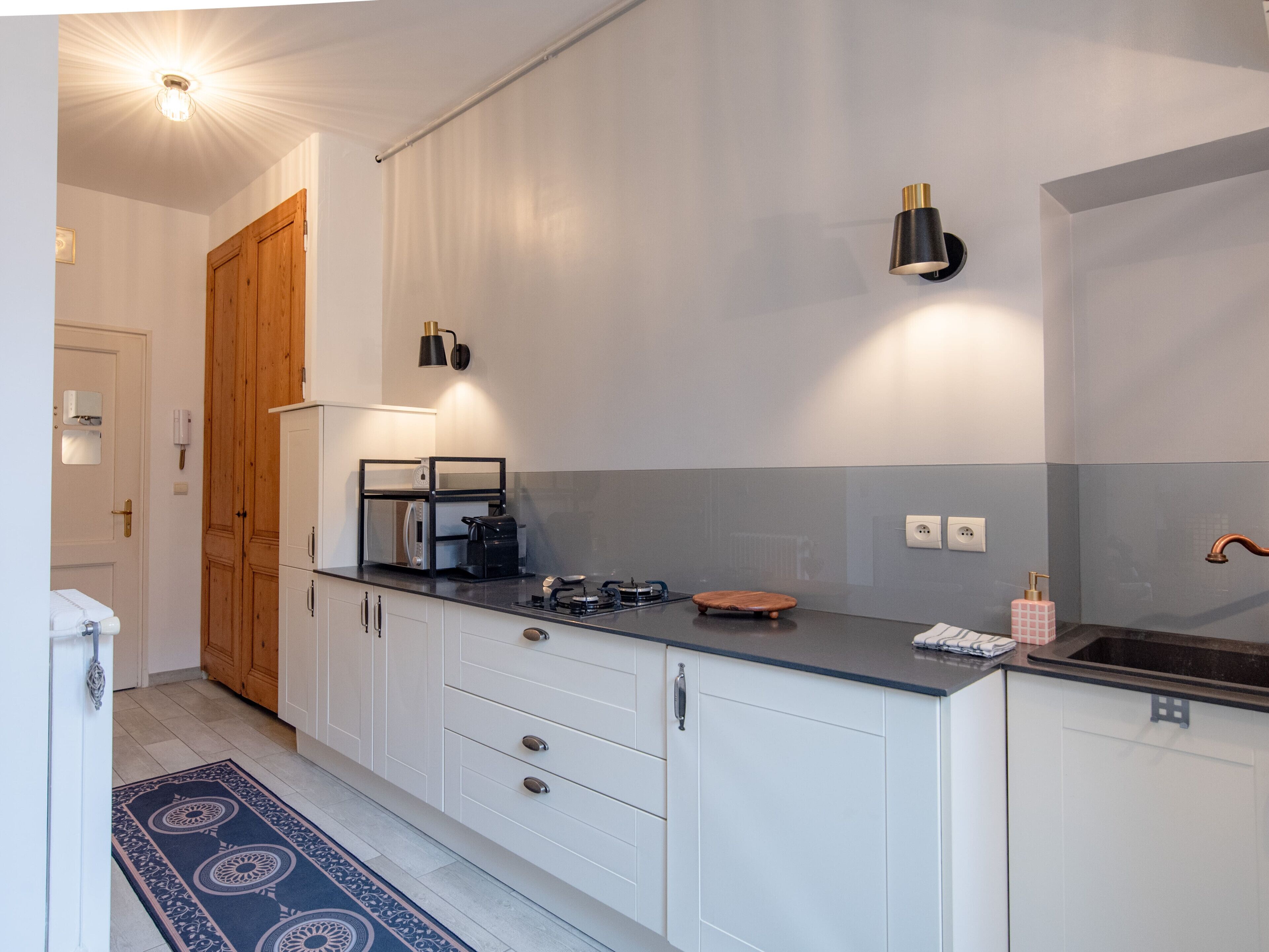 Een moderne keuken met witte kasten, een zwart aanrecht en een houten deur.