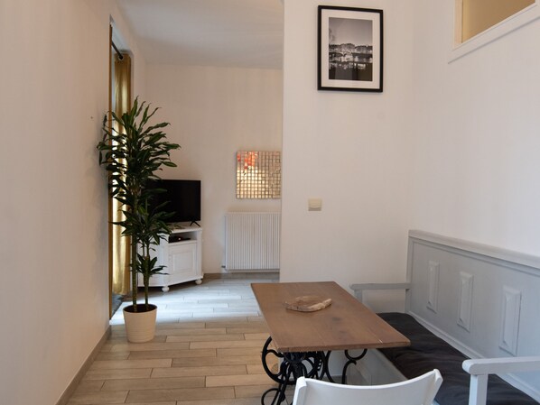 A small dining area with a wooden table and chairs, a potted plant, and a television on a white cabinet.