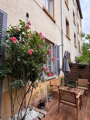 Una terraza de madera con una mesa y sillas, una planta en maceta y un rosal.