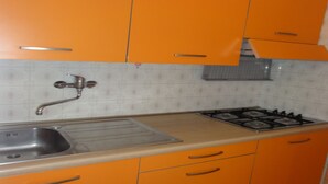 A kitchen with orange cabinets, a stainless steel sink, and a gas stove. - Apartment Close to the Thermal Baths (San Michele al Tagliamento)