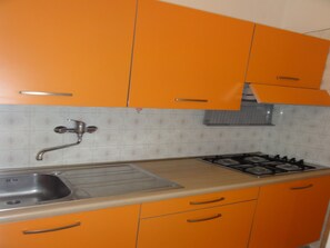 A kitchen with orange cabinets, a stainless steel sink, and a gas stove. - Apartment Close to the Thermal Baths (San Michele al Tagliamento)