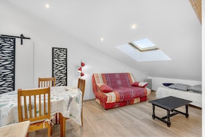 Ein Loft-Zimmer mit Esstisch, zwei Stühlen, einer Couch, einem kleinen Tisch und einem Oberlicht.
