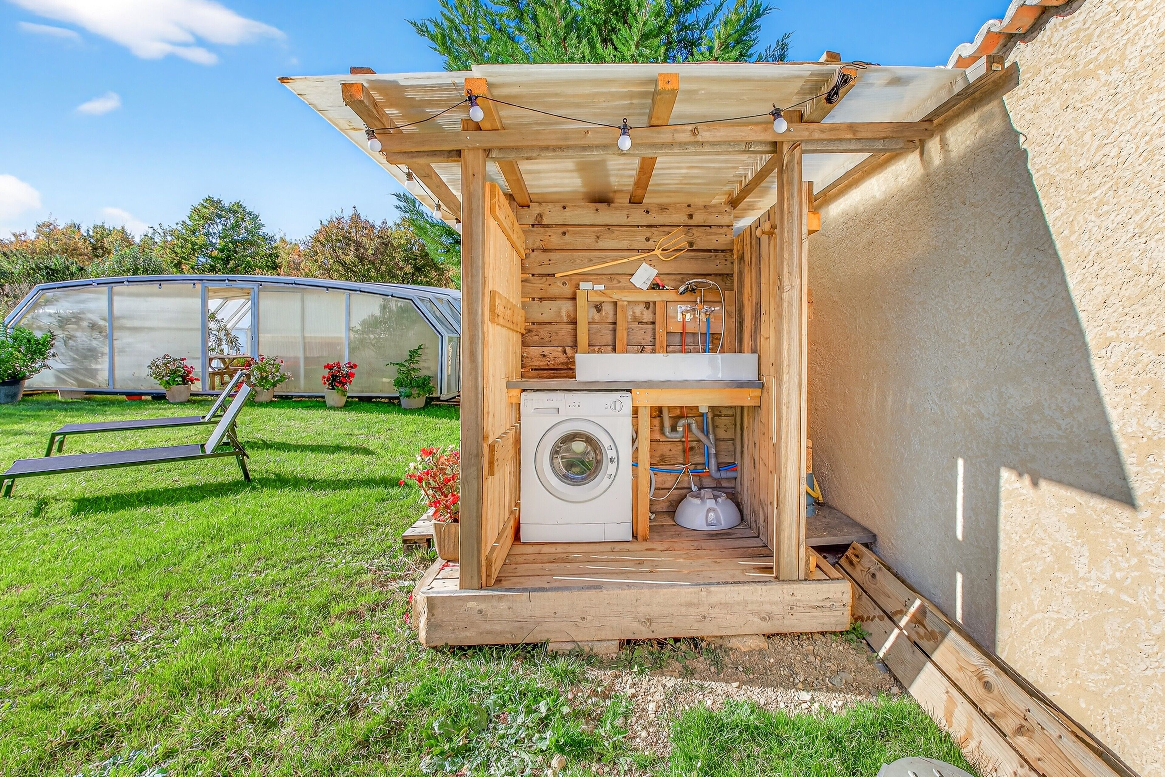 Une petite structure en bois comprenant une machine à laver, une petite table et un banc.