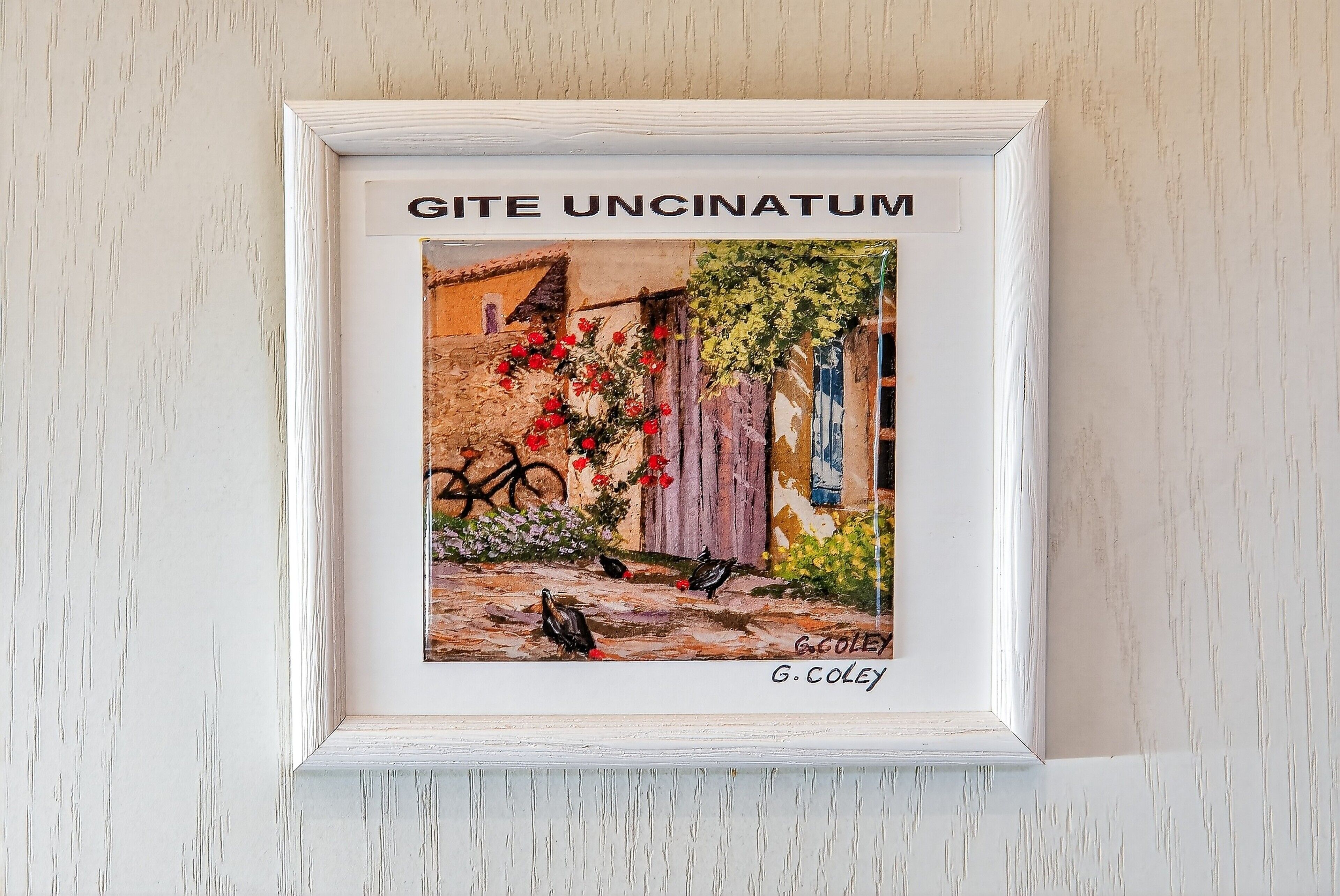 A framed artwork titled 'GITE UNCINATUM' by G. COLEY, depicting a rustic scene with a wooden fence, flowers, and birds.