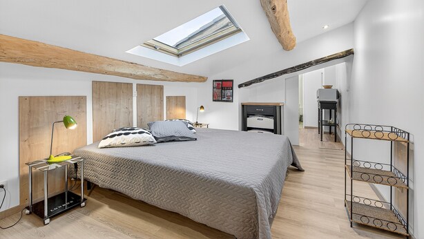 Een moderne slaapkamer met dakraam, een bed met kussens, een bureau met lamp en een rieten plank.