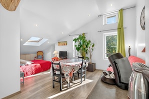 A spacious loft bedroom with a large bed, a dining table, a coffee machine, and a potted plant.