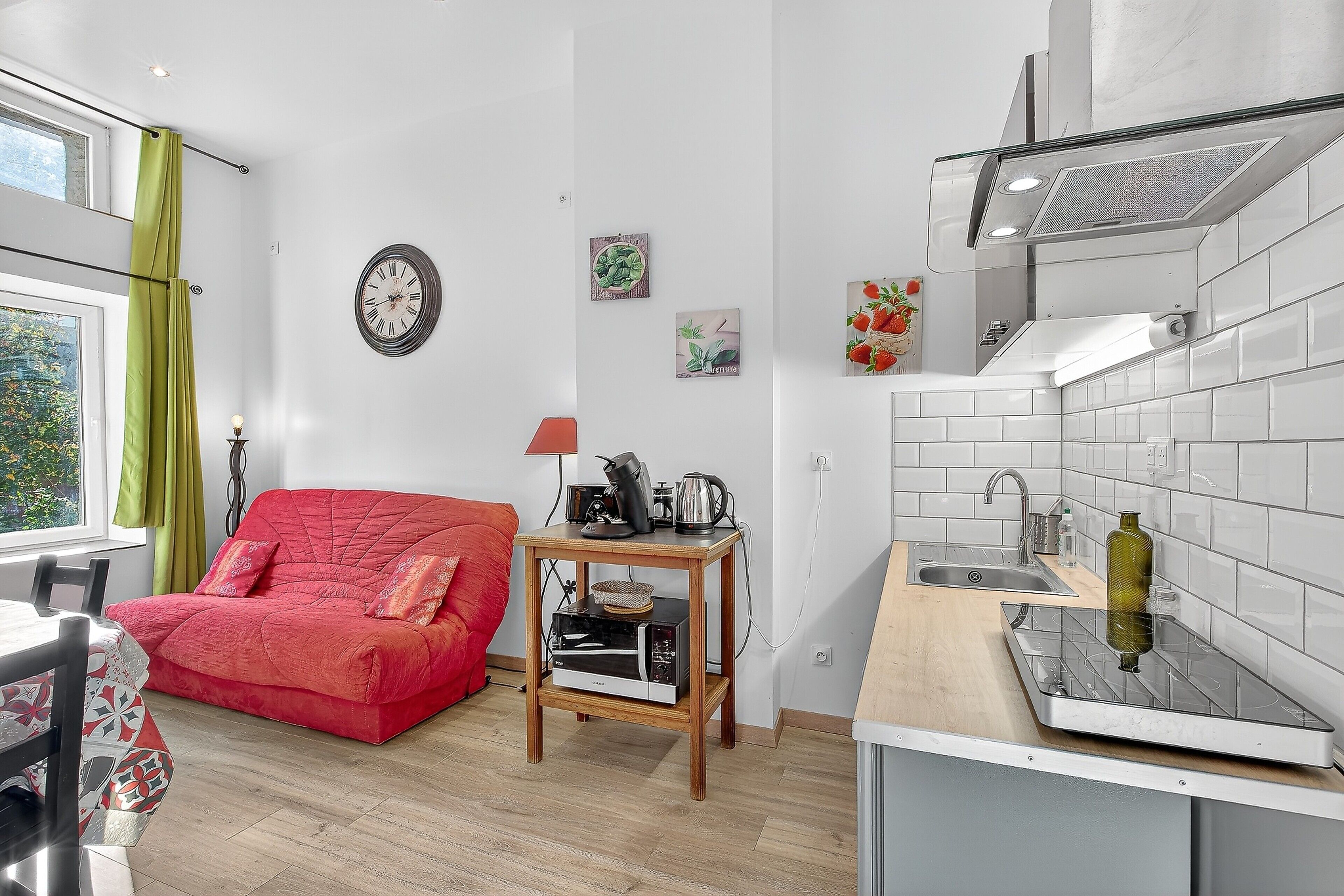 Um espaço de estar compacto com cozinha compacta, um sofá vermelho, uma mesa de jantar e uma janela com cortinas.