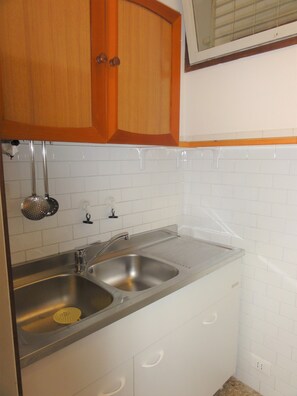 A kitchen with two stainless steel sinks, wooden cabinets, and white subway tiles. - Modern Coastal Apartment (San Michele al Tagliamento)
