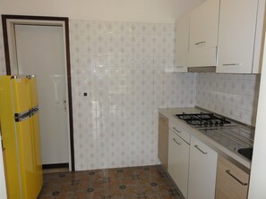 Uma cozinha compacta com geladeira amarela, paredes com azulejos brancos, fogão a gás e pia.