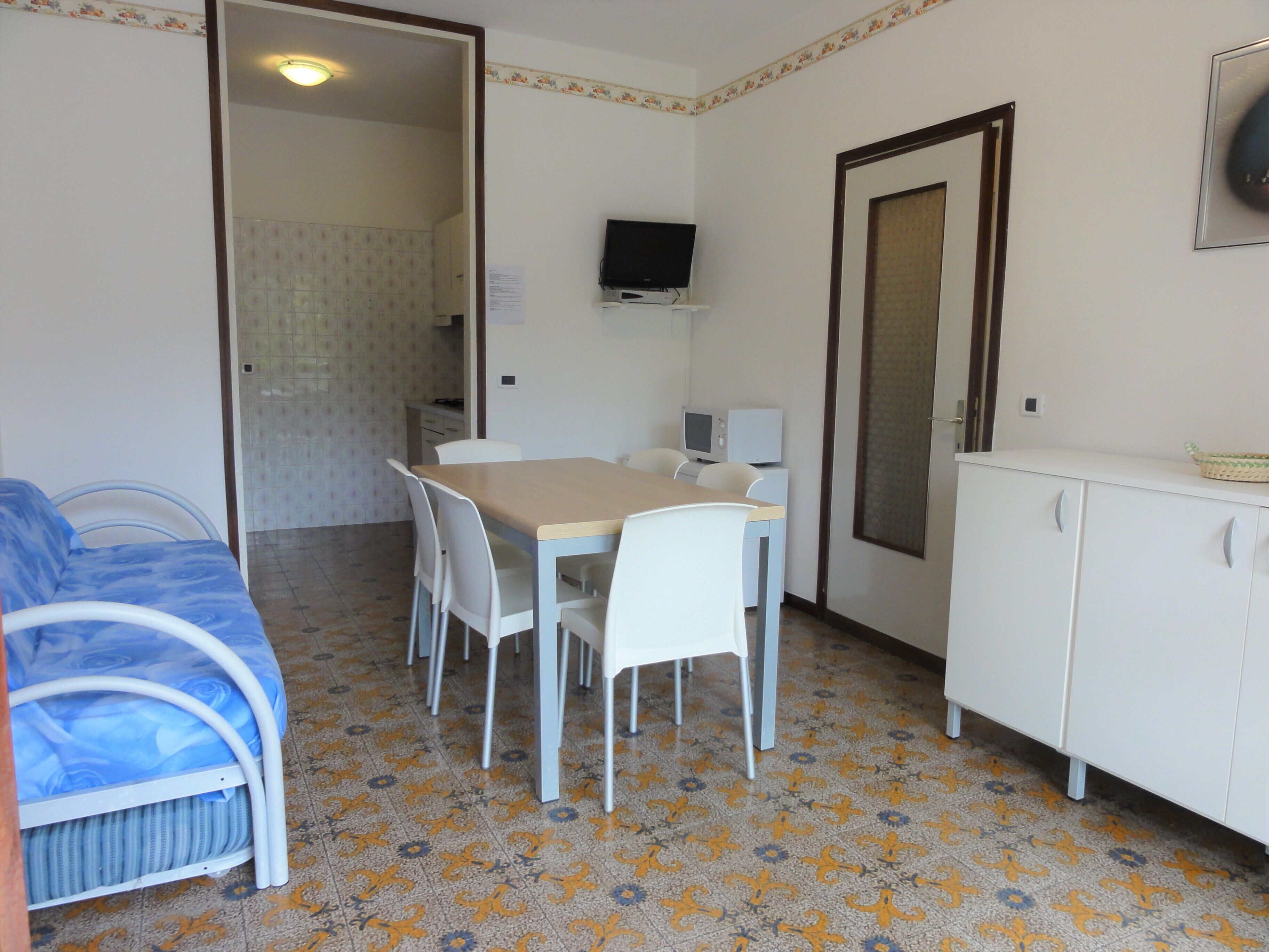 Une petite pièce, de taille modeste, comprenant un lit, une table à manger avec des chaises, un téléviseur fixé au mur et un meuble de rangement.