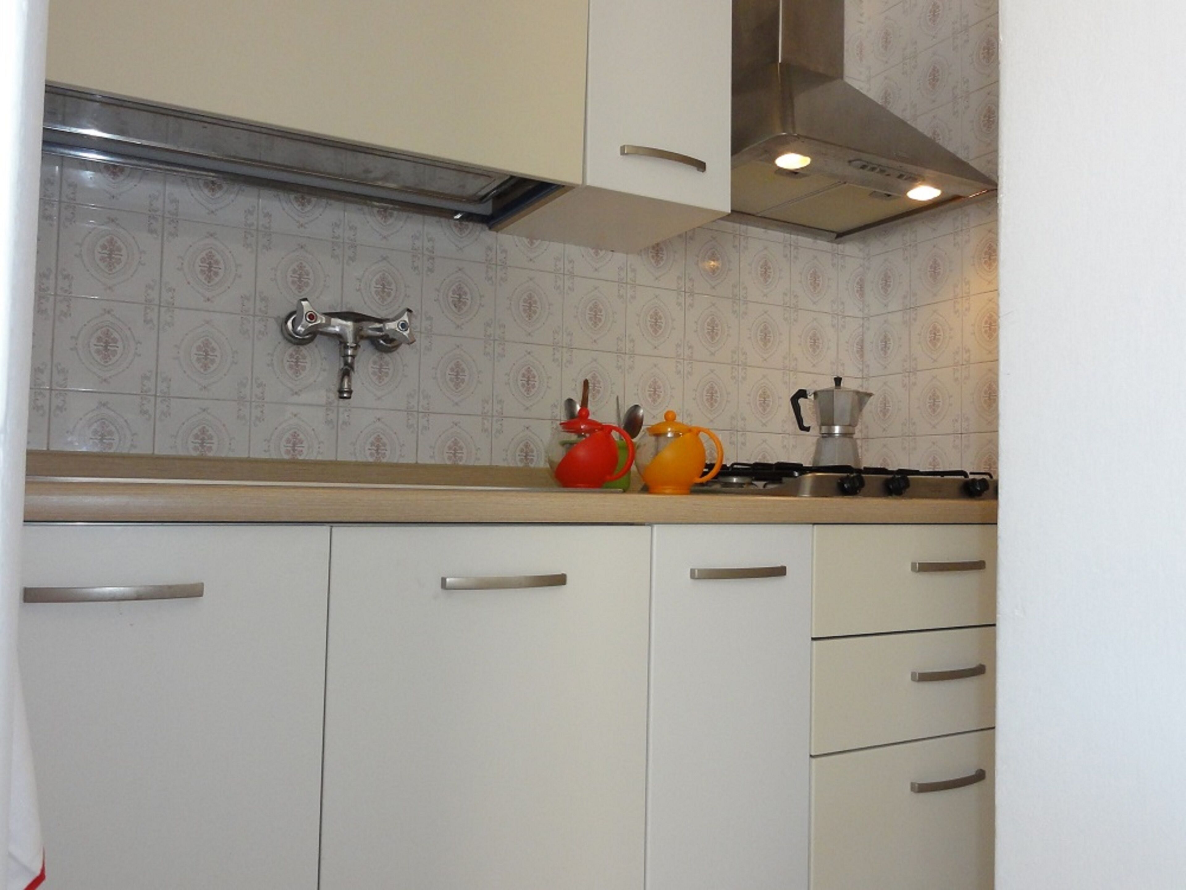 A kitchen with white cabinets, a stainless steel range hood, a gas stove, and a coffee maker.
