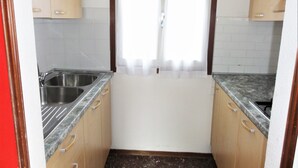 A small kitchen with two sinks, wooden cabinets, and a window with a white curtain. - Quiet Villa Near the Beach (San Michele al Tagliamento)