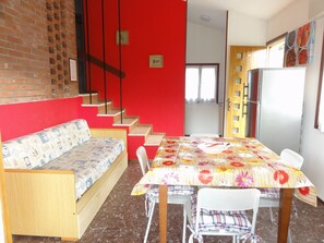 Un área de comedor con una mesa, sillas y un sofá. Una escalera conduce a otra habitación.