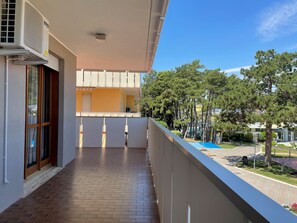 Un balcón con piso de baldosas, una ventana con vista a un edificio y un cielo despejado.