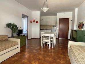 A living room with a sofa, a dining table with chairs, a green cabinet, and a plant. - Apartment Near Shops and Beach (San Michele al Tagliamento)