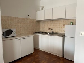 A compact kitchen with white cabinets, a microwave, a stove, and a refrigerator. - Apartment Near Shops and Beach (San Michele al Tagliamento)
