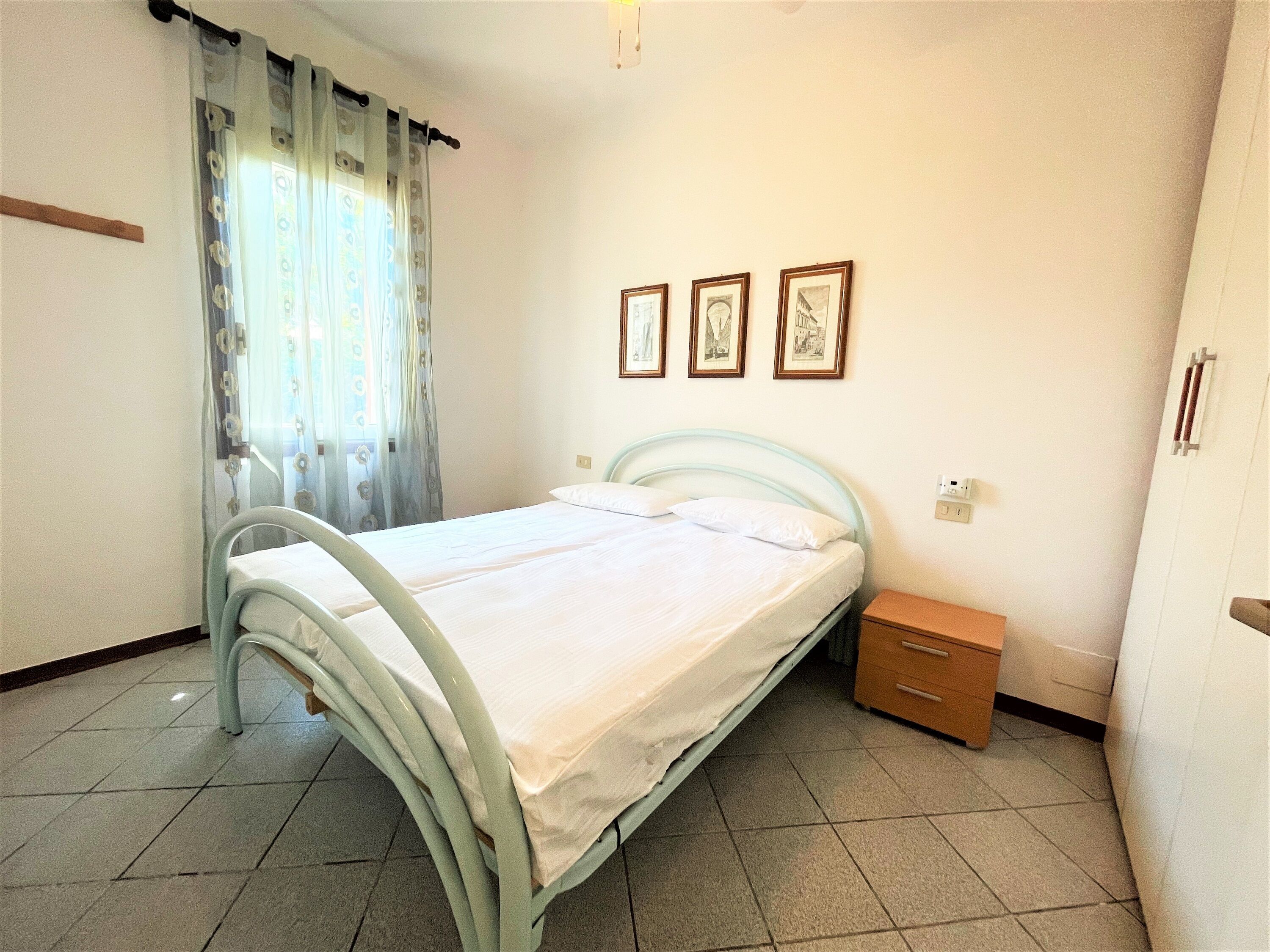 Een slaapkamer met een bed, een nachtkastje en drie ingelijste foto’s aan de muur.