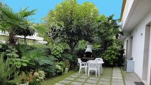 Un giardino con vialetto in pietra, sedie bianche e forno a legna.