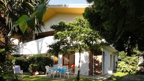 A small house with a patio, surrounded by lush greenery and a well-maintained lawn.