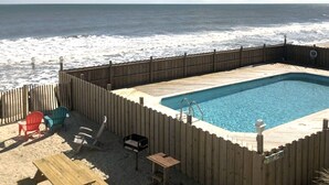 Una terraza de madera con piscina, sillas y una mesa, con vista al océano.