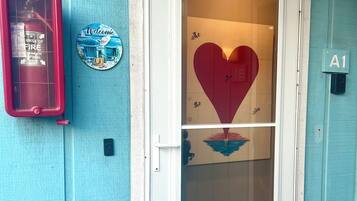 Una puerta con un ventanal en forma de corazón, un extintor, un letrero de bienvenida y un felpudo.