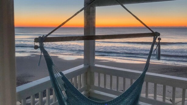 Una hamaca en un balcón con vista al océano al atardecer.