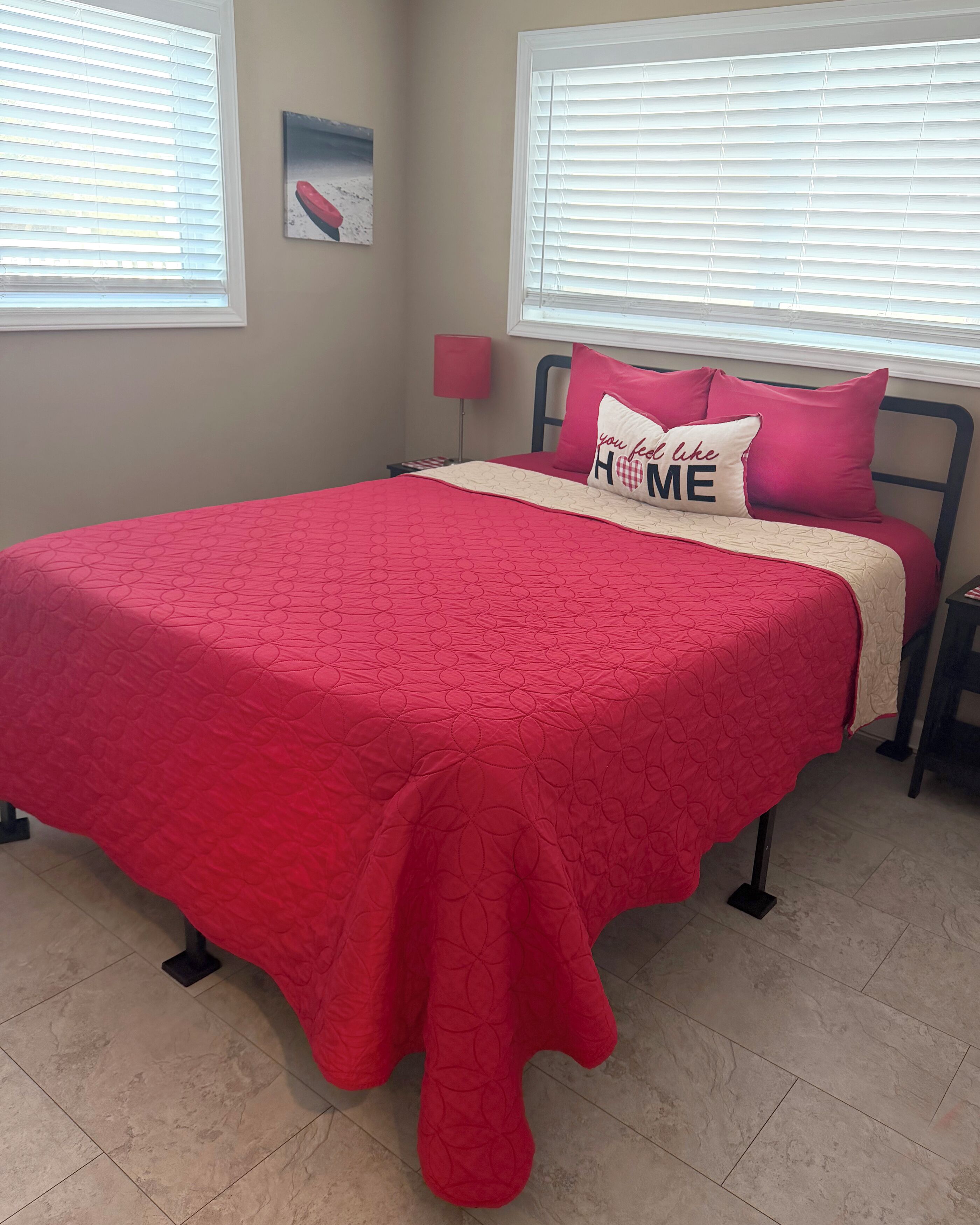 A bedroom with a red bedspread, a pillow with 'you feel like HOME' text, and a painting on the wall.