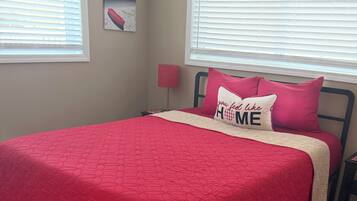 A bedroom with a red bedspread, a pillow with 'you feel like HOME' text, and a painting on the wall.