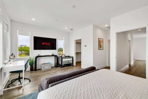 Una habitación de hotel moderna con una cama grande, un escritorio con computadora, un televisor montado en la pared y vistas al exterior.