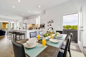 Una cocina moderna con armarios blancos, un comedor con mesa para cuatro y un balcón con vistas.