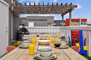 Un área de comedor al aire libre con una mesa lista para dos personas, rodeada de sillas y una pérgola en lo alto.