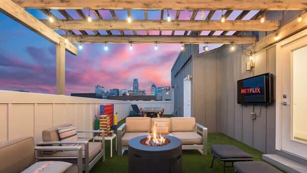 A rooftop patio with a fire pit, outdoor seating, and a view of the city skyline at dusk. - Designer Dallas Home, Rooftop, Kid Friendly Stay (Dallas)