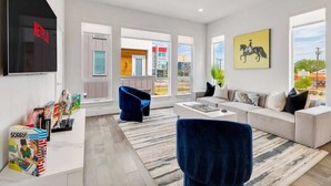 A modern living room with a sofa, a blue chair, a coffee table, and a TV mounted on the wall. - Designer Dallas Home, Rooftop, Kid Friendly Stay (Dallas)