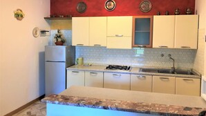 A kitchen with white cabinets, a gas stove, a sink, and decorative plates on the wall. - Apartment With Garden in Bibione (San Michele al Tagliamento)