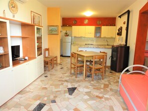 Una cocina compacta con comedor, que presenta suelo de baldosas, mobiliario de madera y un refrigerador.