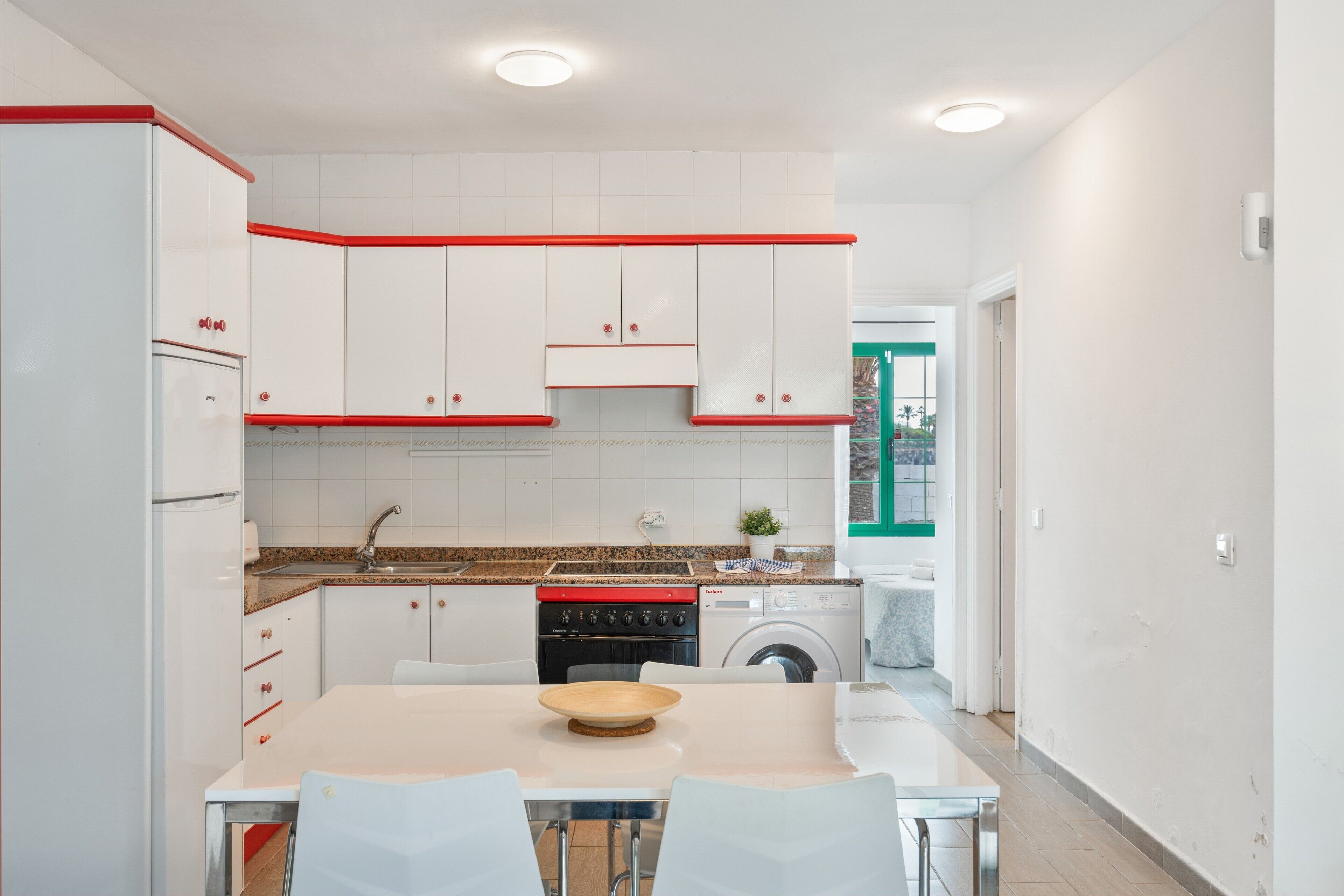 A modern kitchen with white cabinets, a red countertop, and a dining area with a table and chairs.