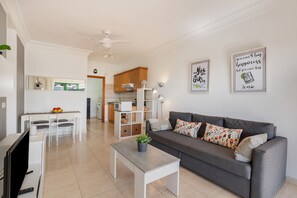 A modern living room with a grey sofa, a white coffee table, and a dining area with a white table and chairs.
