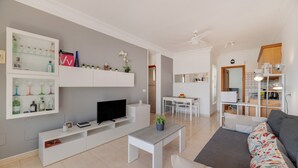 Una sala de estar moderna con una televisión de pantalla plana, un mueble blanco para entretenimiento, un sofá gris y un comedor con una mesa y sillas.