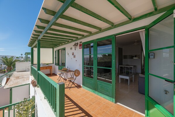 A covered outdoor area with a dining table and chairs, a small kitchen area, and a balcony with a railing.