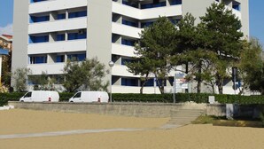 A multi-story building with a flat facade, several balconies, and a parking area with white vans. - Bright Flat With a Large Balcony (San Michele al Tagliamento)