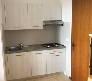 Una cocina moderna con armarios de madera clara, un lavamanos de acero inoxidable y una estufa a gas.