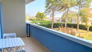 Een balkon met een tafel en stoelen, met uitzicht op een aangelegde tuin en een parkeerplaats.