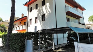 A multi-story building with a flat roof, a balcony on the upper floor, and a covered outdoor area.